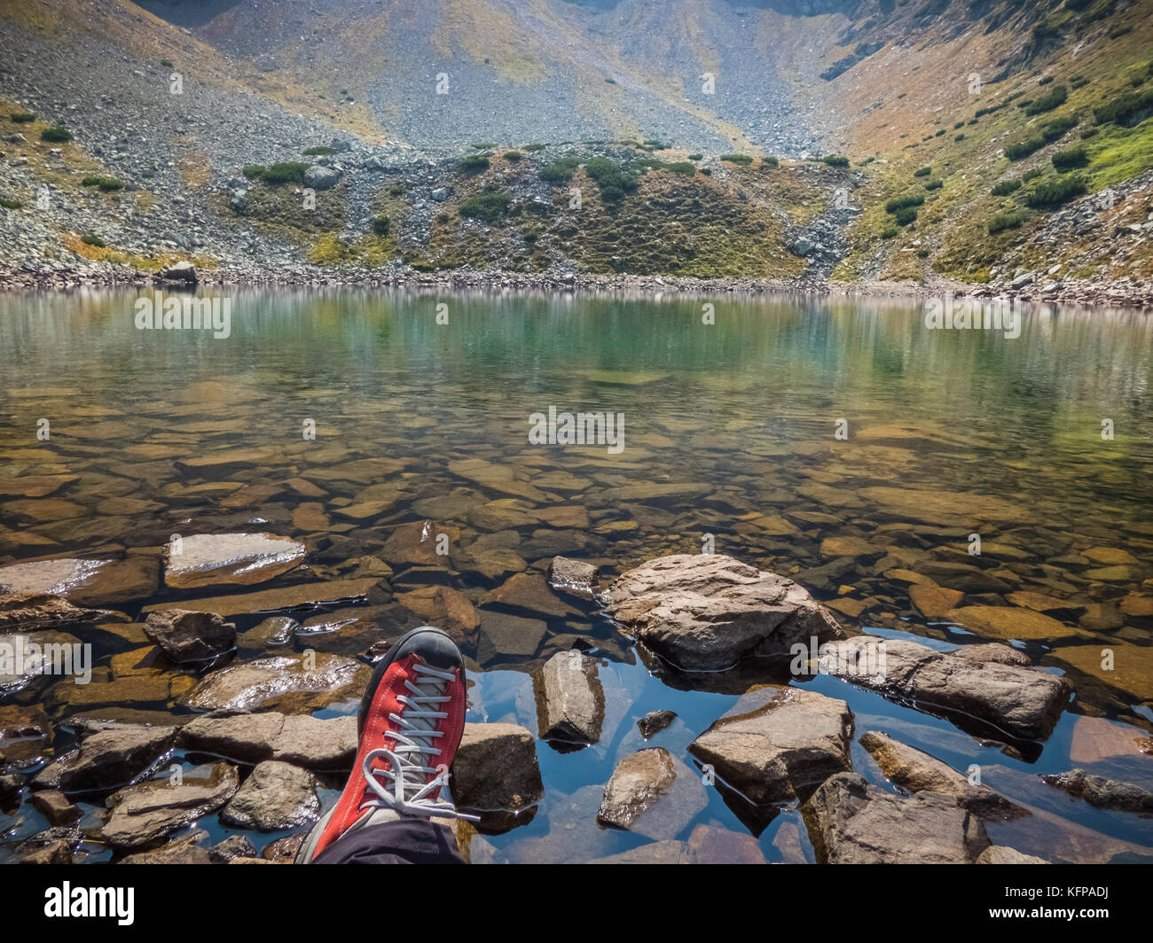 Wet rocks and a hiking boot at the shore of a glacial lake high in the wilderness of the Carpathian Mountains. Stock Photo
