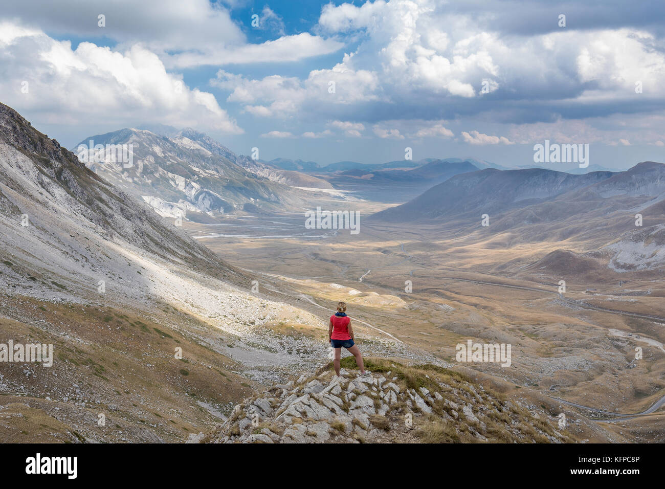 Woman staying at rock and watching power of nature at mountains of Gran Sasso National Park, Abruzzo, Italy Stock Photo