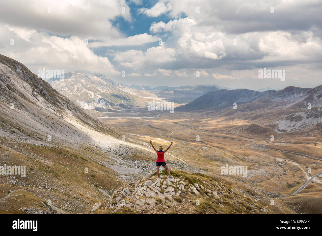 Happy woman with raised hands staying on rock formation and watching power of nature - plateau of Campo Imperatore, Abruzzo, italy Stock Photo