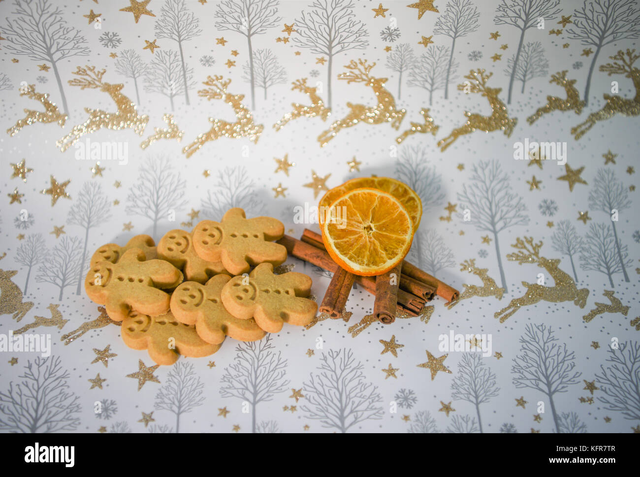 colorful Christmas food photography image with mini ginger bread man biscuits and cinnamon orange slice with gold glitter reindeer xmas wrapping paper Stock Photo