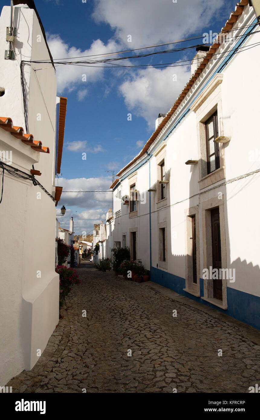 Narrow street of cobblestone and white houses of blue bands leading to the castle at the historical village of Terena. Alentejo, Portugal. Stock Photo