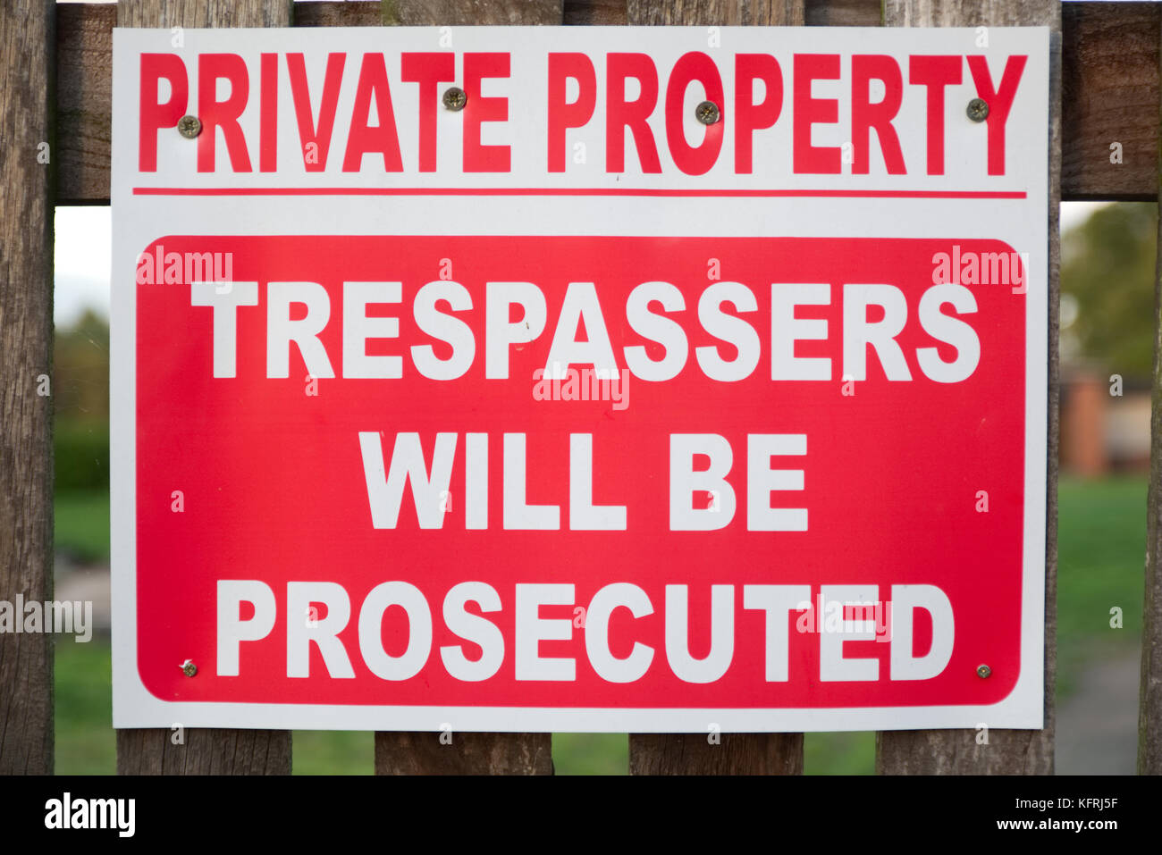 Red and white private property trespassers will be prosecuted sign screwed on a wooden fence Stock Photo