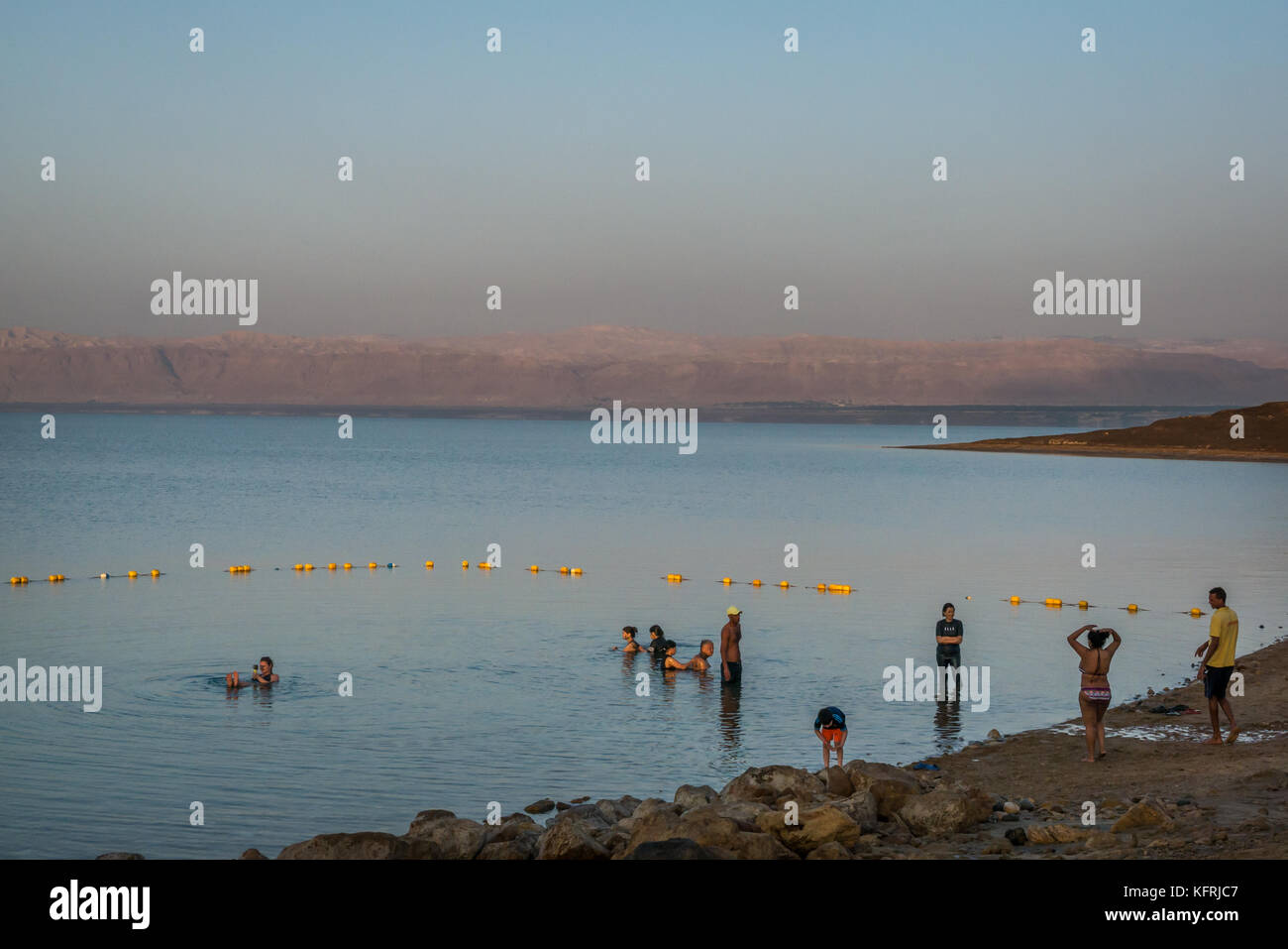 Early morning, Holiday Inn Dead Sea beach resort, Jordan with people  covered in mud and floating in salty water, and view over Dead Sea to West Bank Stock Photo