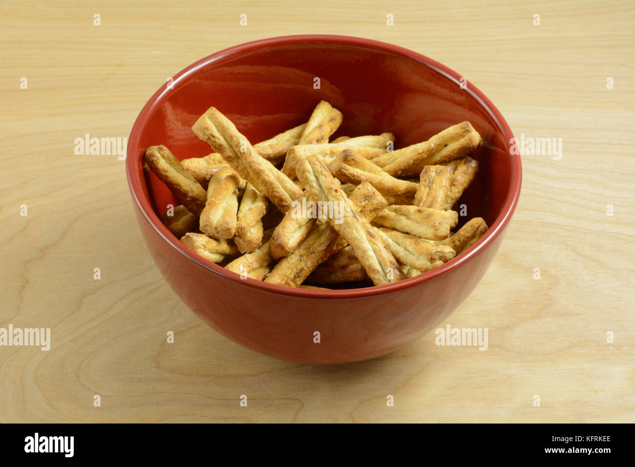 Braided honey pretzel sticks snack in red bowl on wooden table Stock Photo