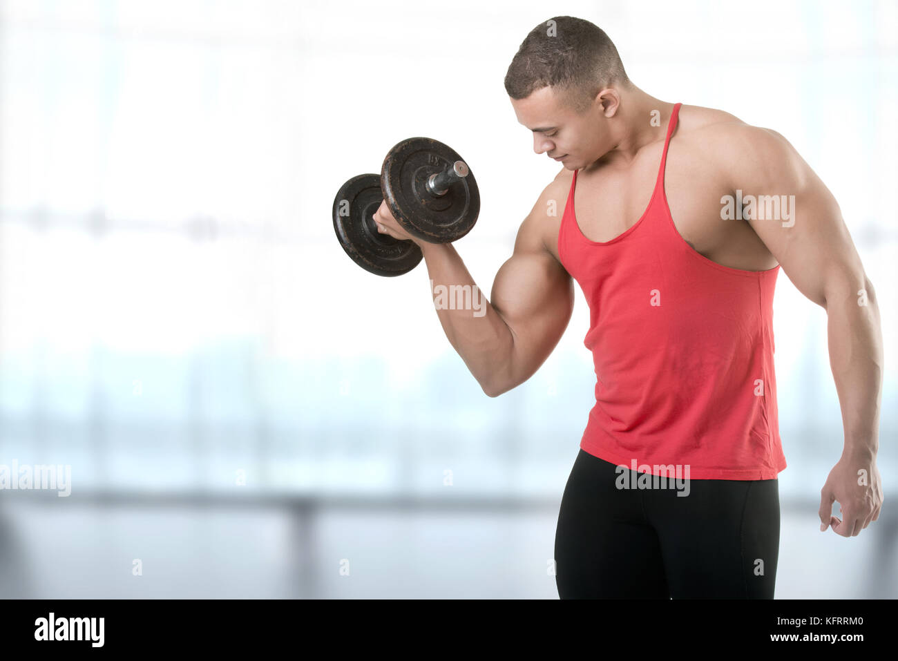 Fit athlete doing standing dumbbell curls for training his biceps, in a blue background Stock Photo