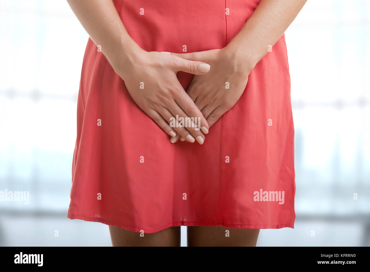 Close up of a woman with hands holding her crotch, in a blue background Stock Photo