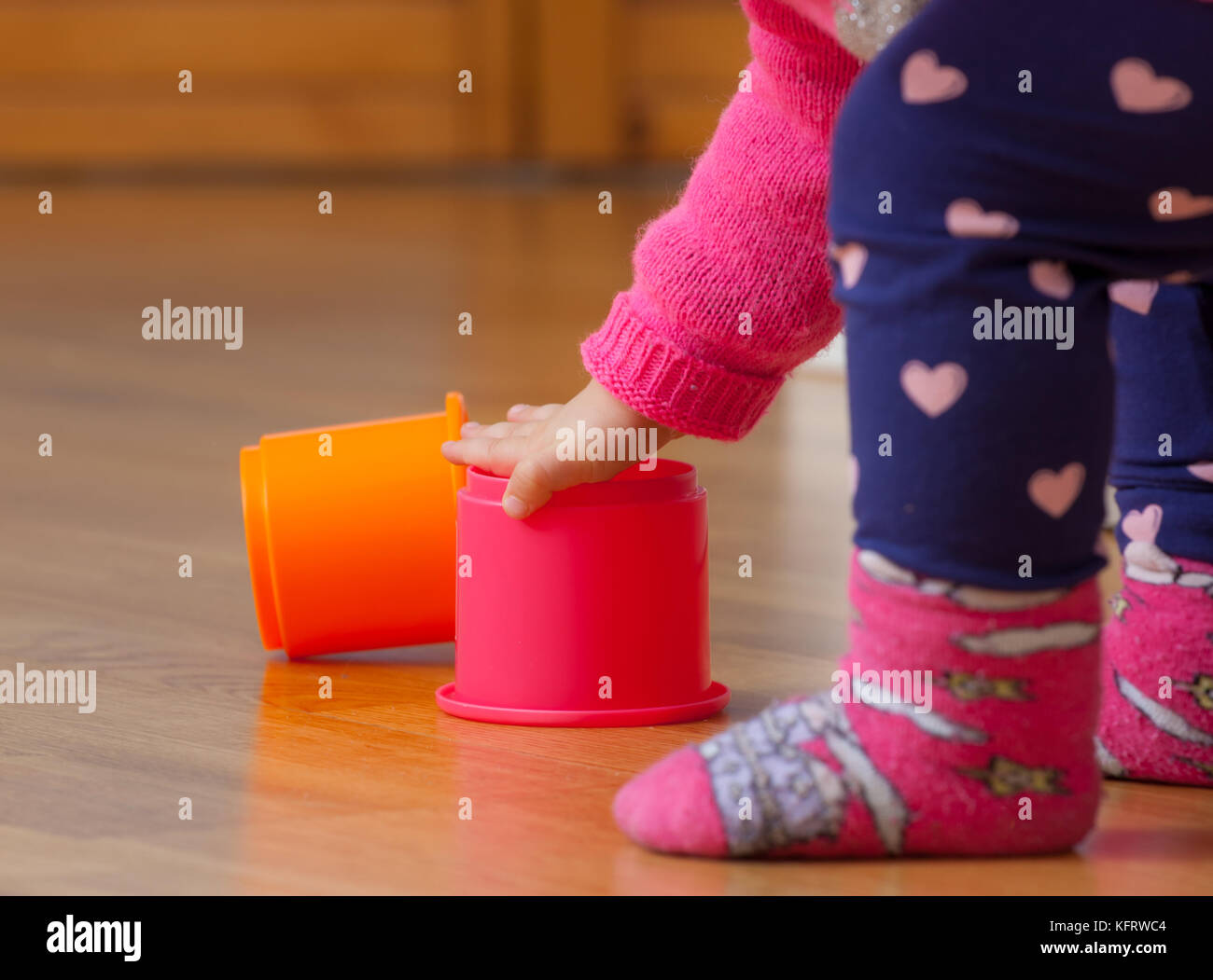 Toddler baby girl plays with colored cups, toy for cognitive development. Stock Photo