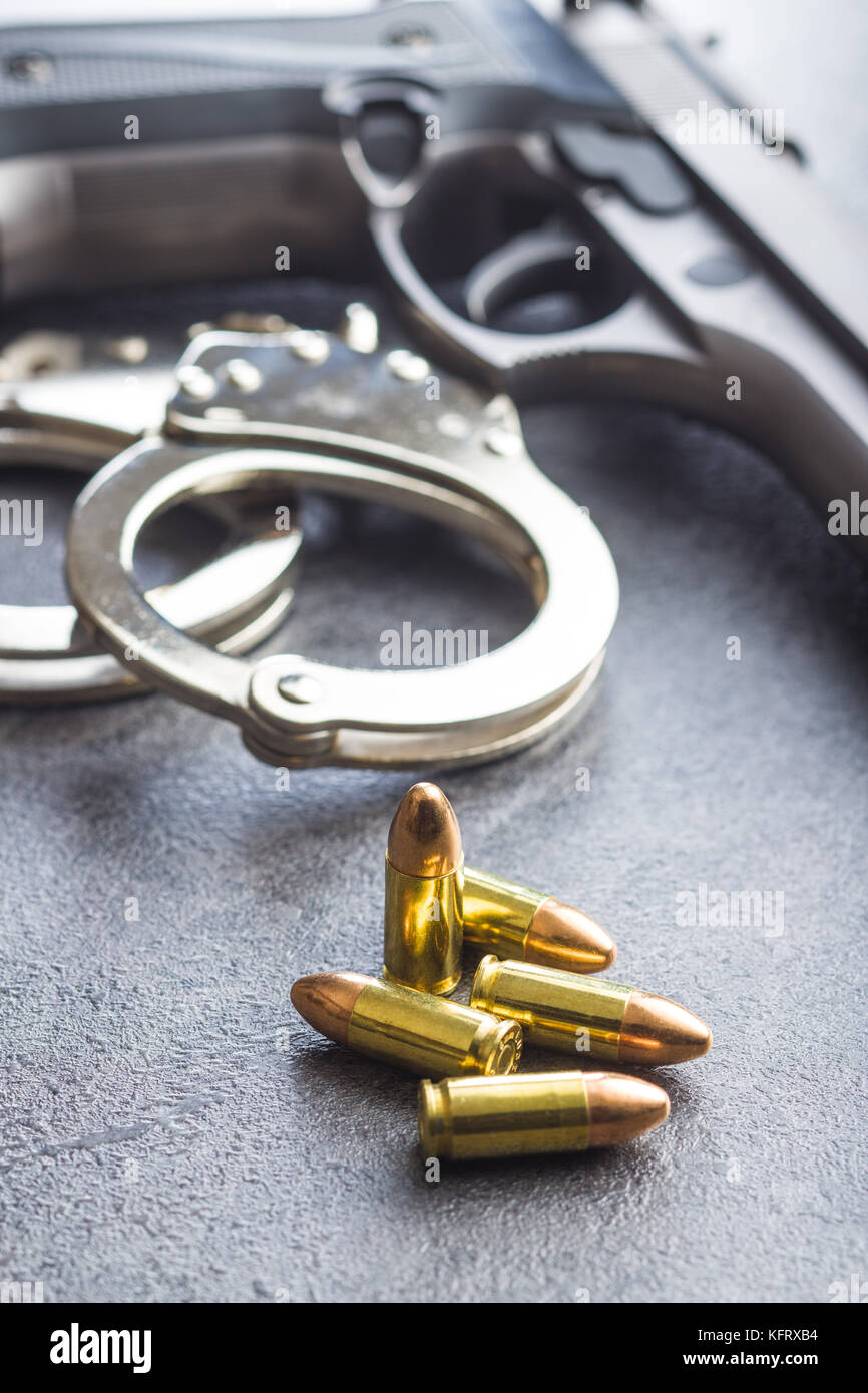 Pistol bullets, handgun and handcuffs on black table. Stock Photo