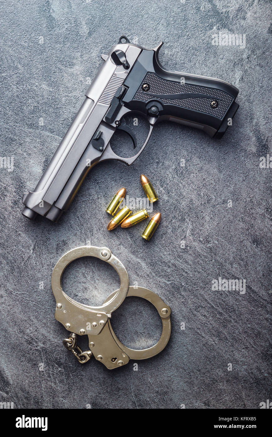 Pistol bullets, handgun and handcuffs on black table. Stock Photo