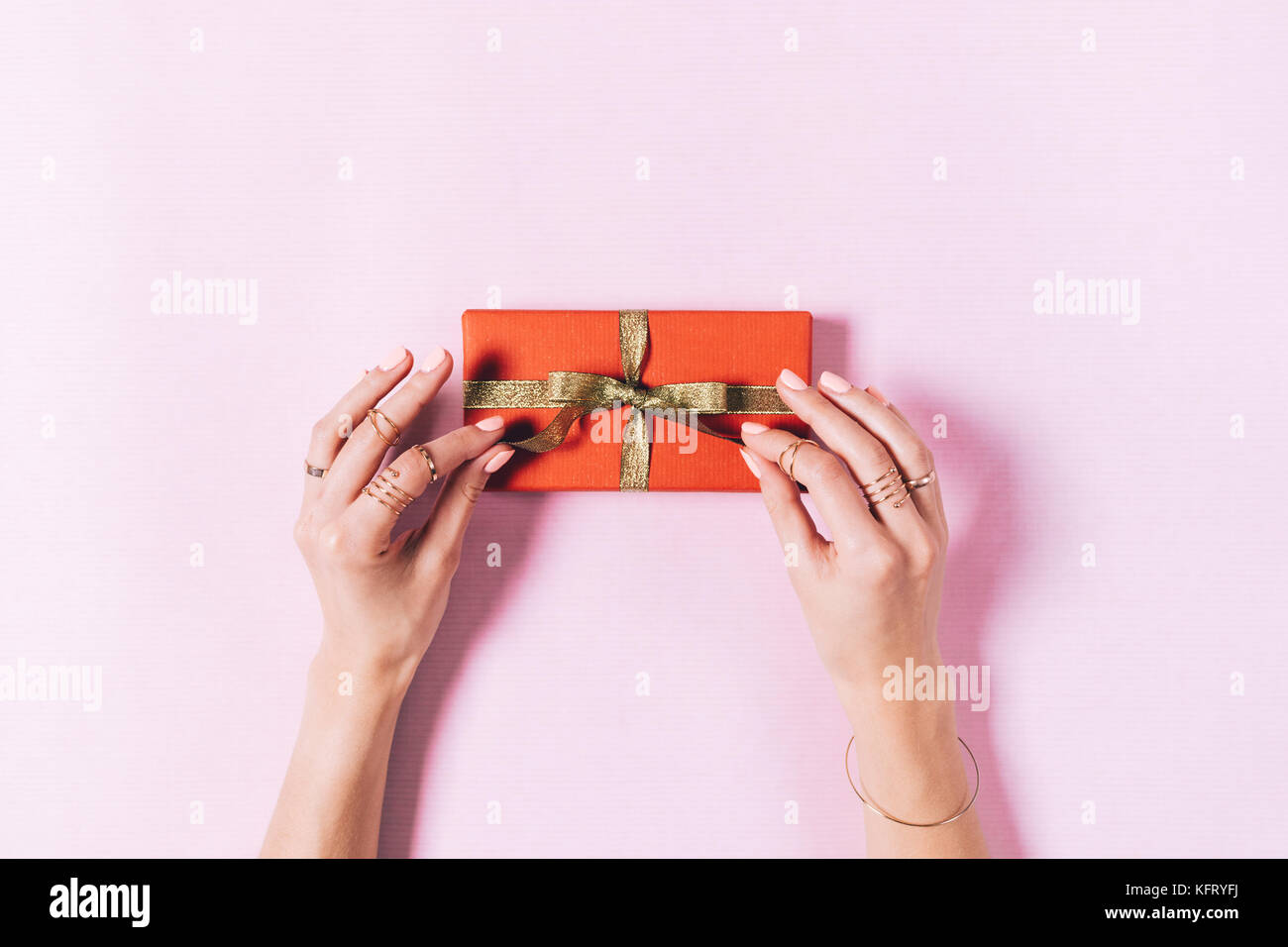 Top view of female hands tying a bow on a box with a gift on a pink background Stock Photo