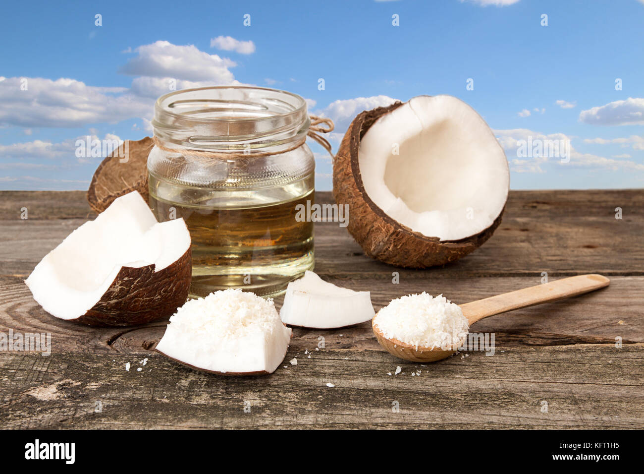 Halfs of coconut, jar of coconut oil, coconut flakes on blue cloudy sky