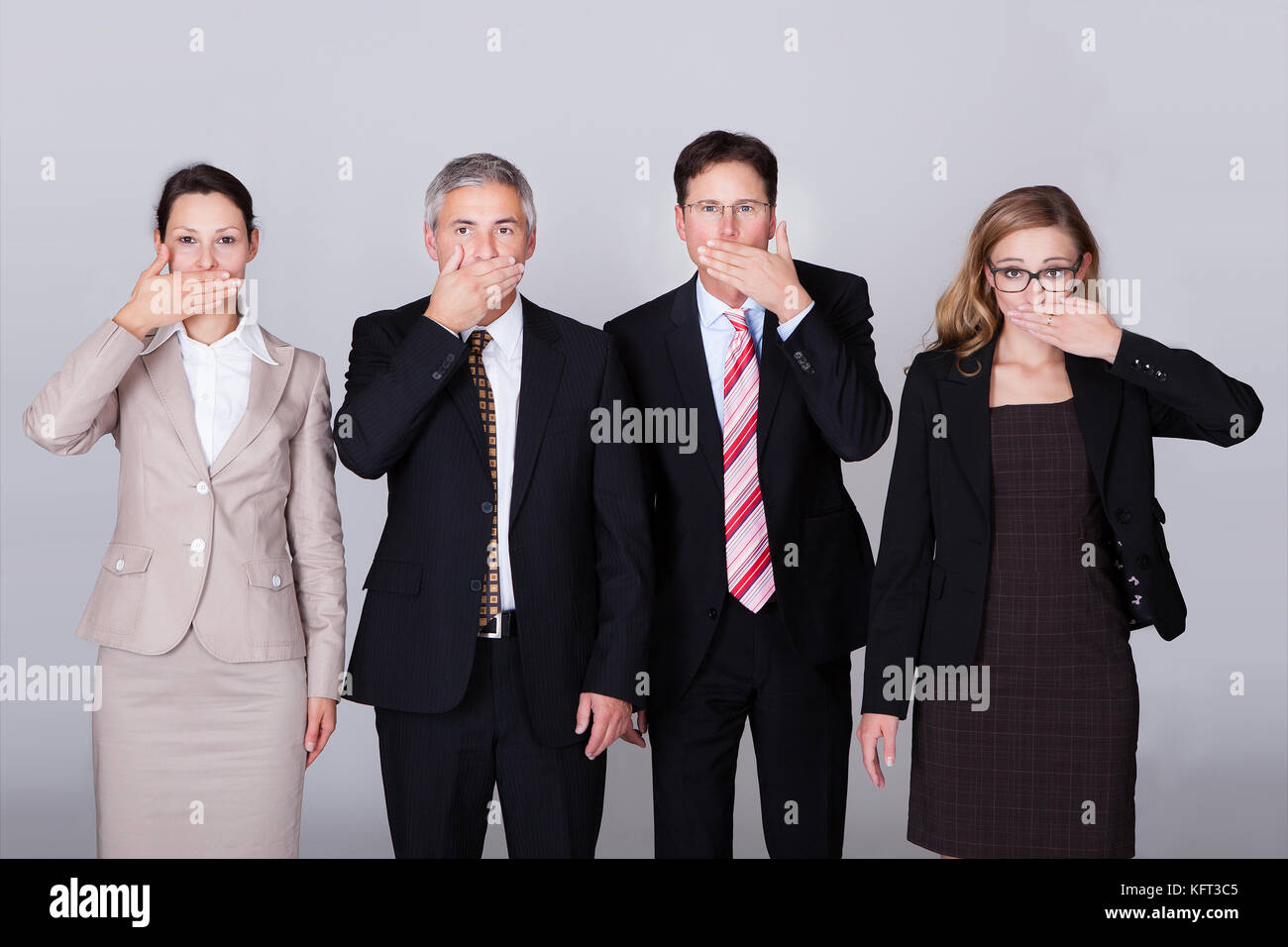Four diverse businesspeople standing in a row gesturing for silence in