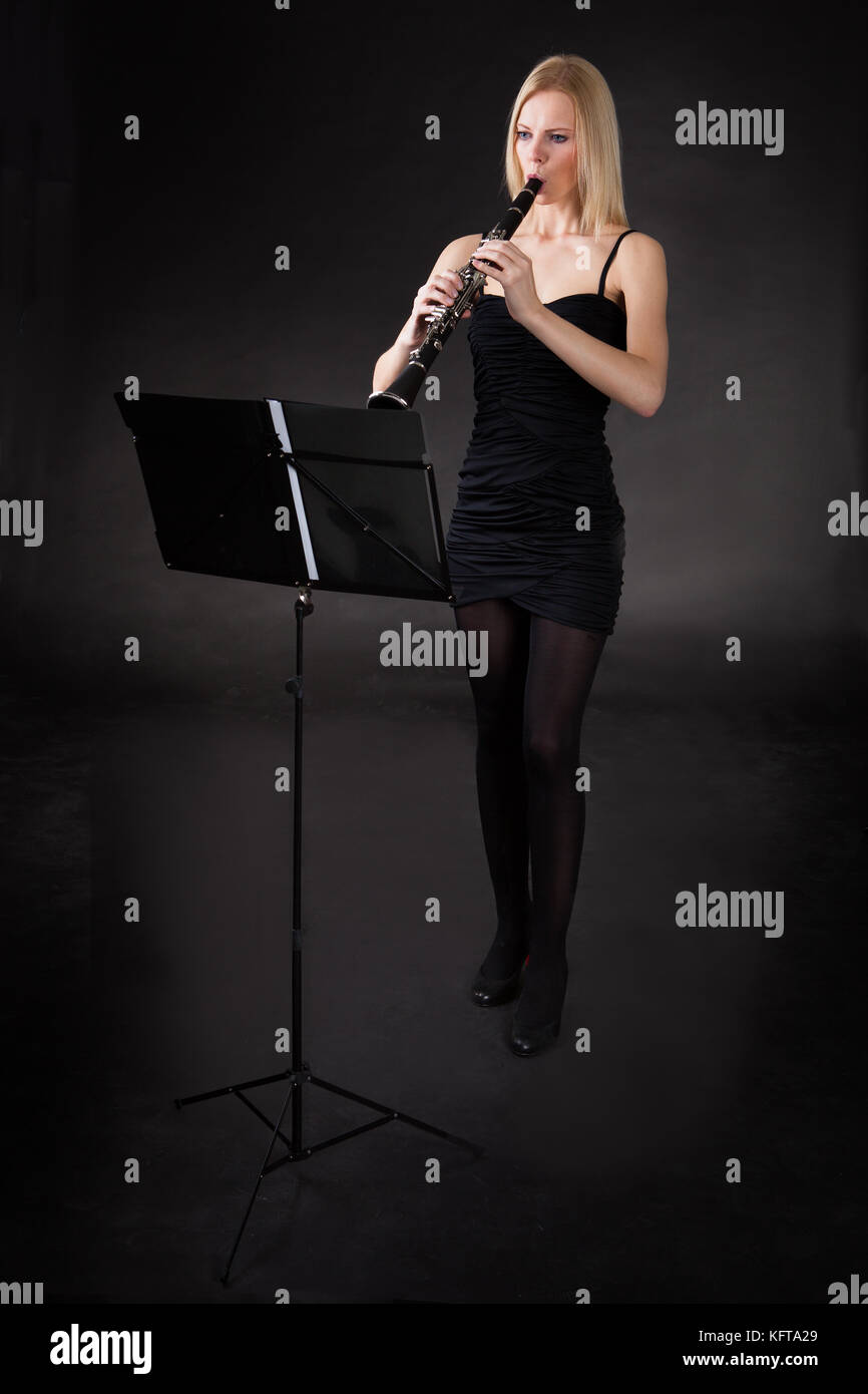 Beautiful young woman playing clarinet over black background Stock Photo