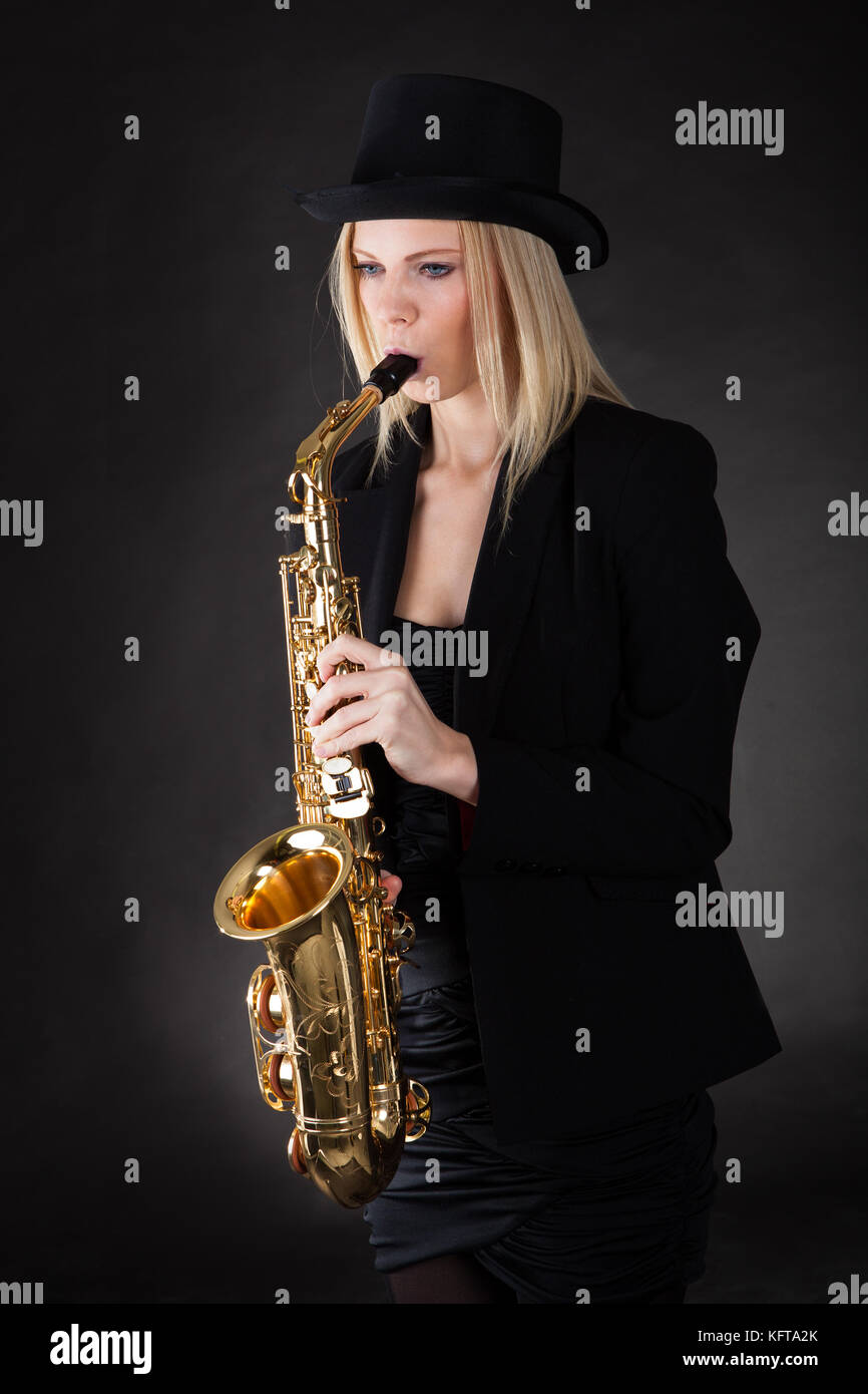 Beautiful young woman playing saxophone over black background Stock Photo