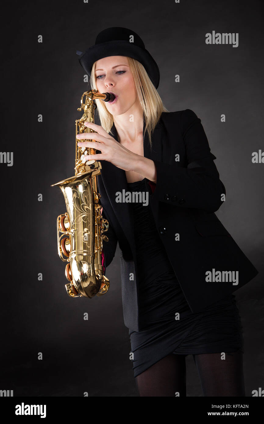 Beautiful young woman playing saxophone over black background Stock Photo