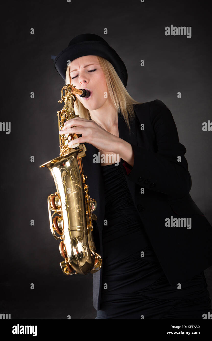 Beautiful young woman playing saxophone over black background Stock Photo
