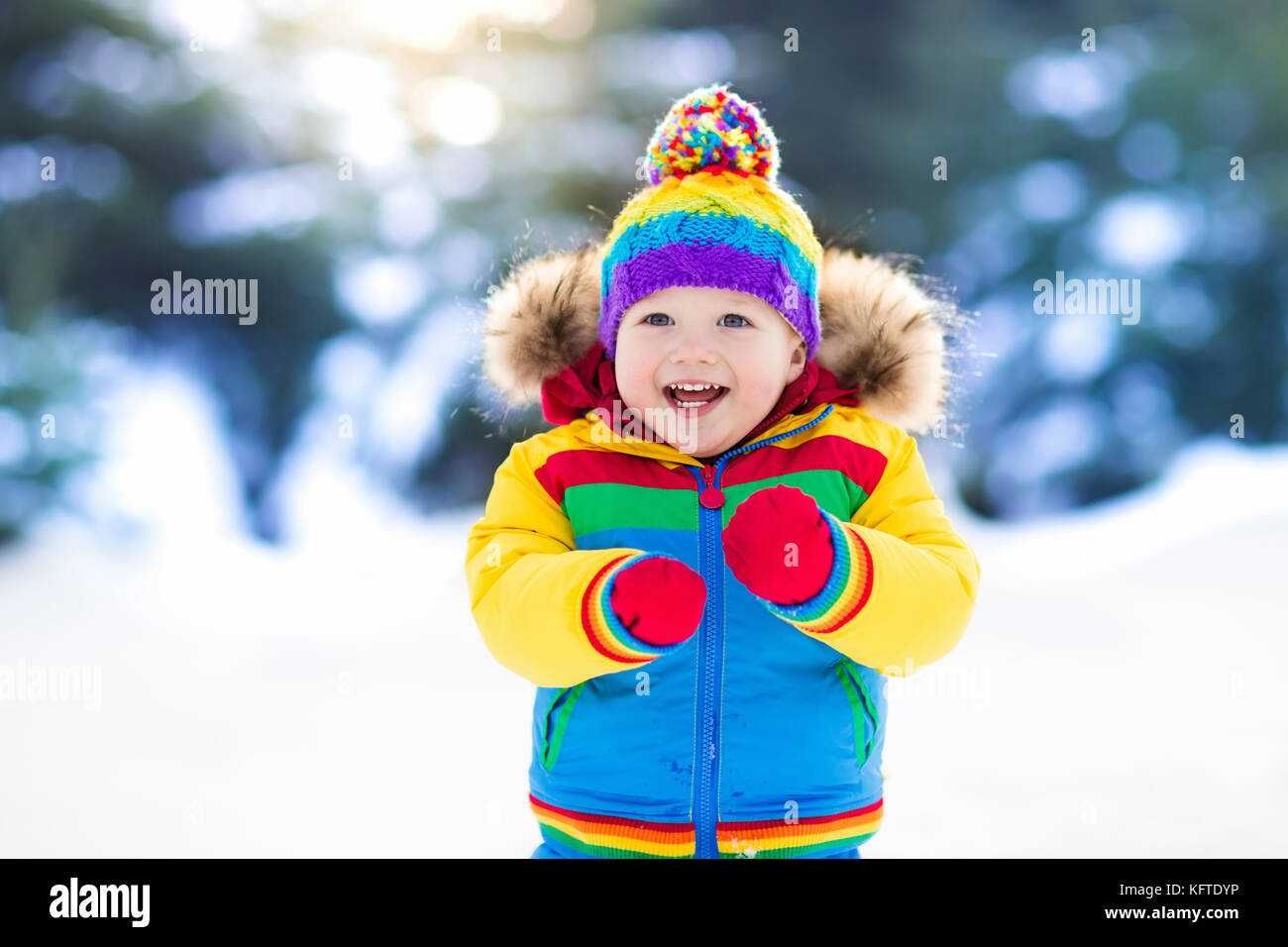 Child playing with snow in winter. Little boy in colorful jacket and ...
