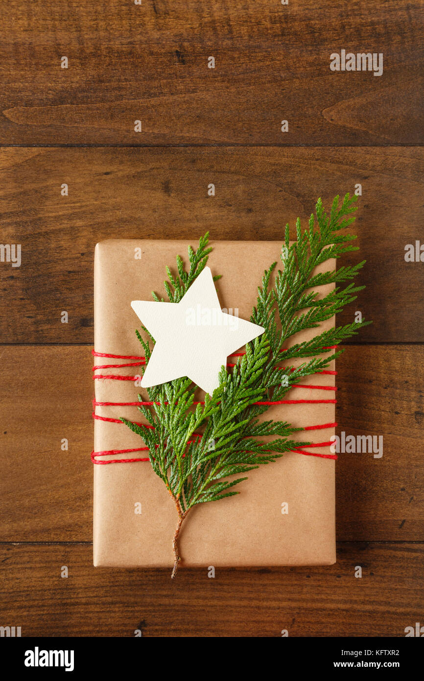 Christmas gift present wrapped in recycled wrapping paper with natural evergreen decorations and a blank, star-shaped gift tag on wood background Stock Photo