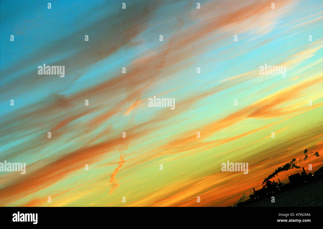 Silhouette of industrial building emitting smoke at sunset with colorful sky. Stock Photo