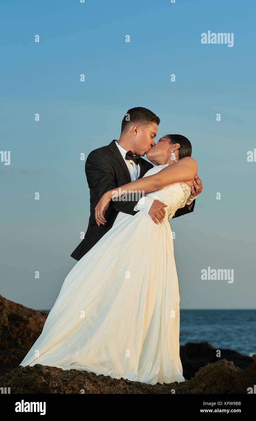Groom kissing bride on blue sky background at ocean beach Stock Photo ...