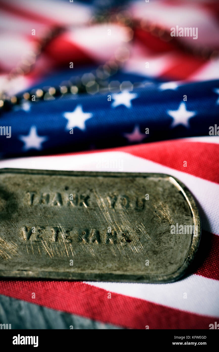 closeup of a rusty dog tag with the text thank you veterans engraved in it, next to a flag of the United States, on a rustic wooden surface Stock Photo
