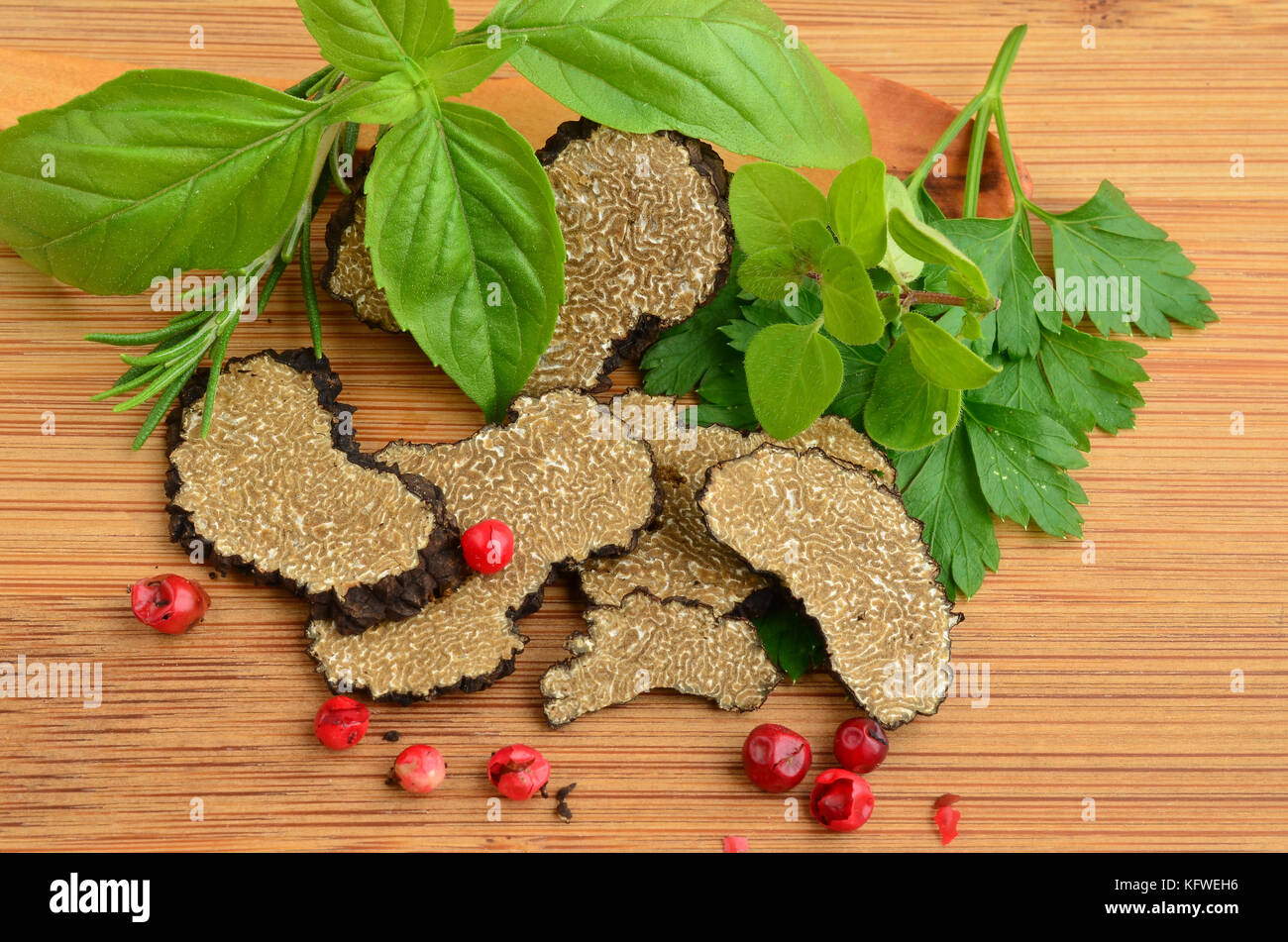 Sliced black truffle with fresh, green aromatic plants and red pepper on wooden background Stock Photo