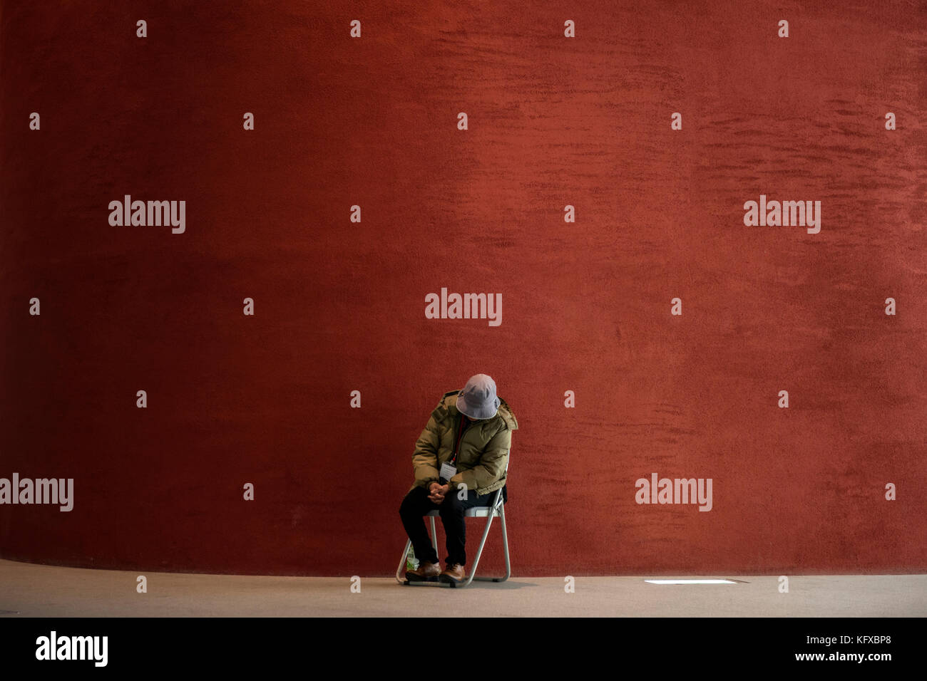 A person sleeping against a red wall Stock Photo
