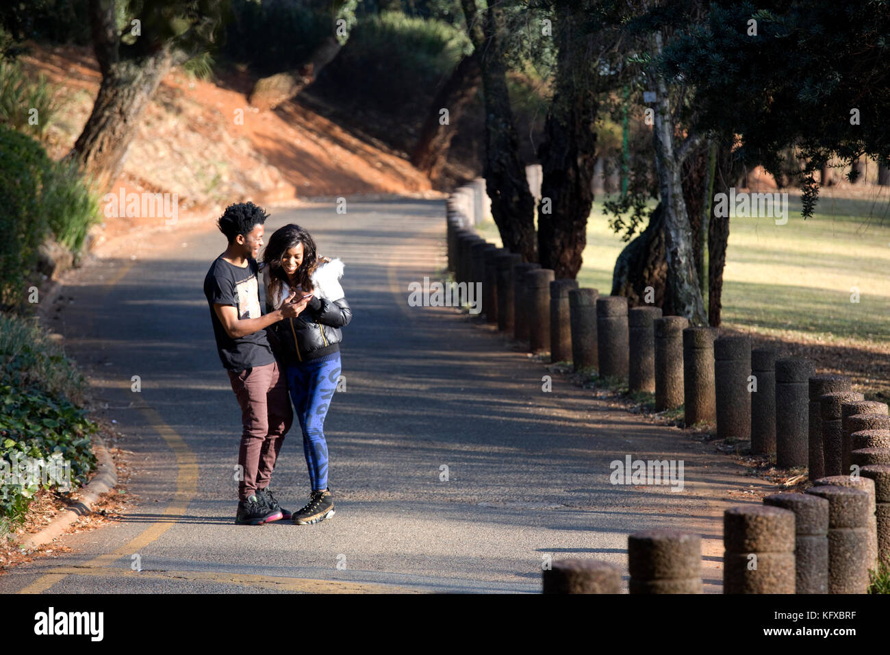 Couple looking at a cellphone whilst walking down a road Stock Photo
