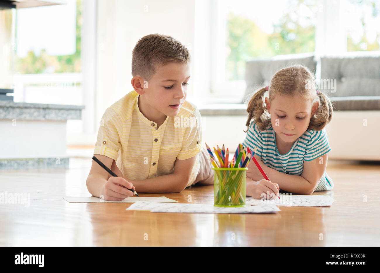 Two cute children draws with colorful pencils on the floor at home ...