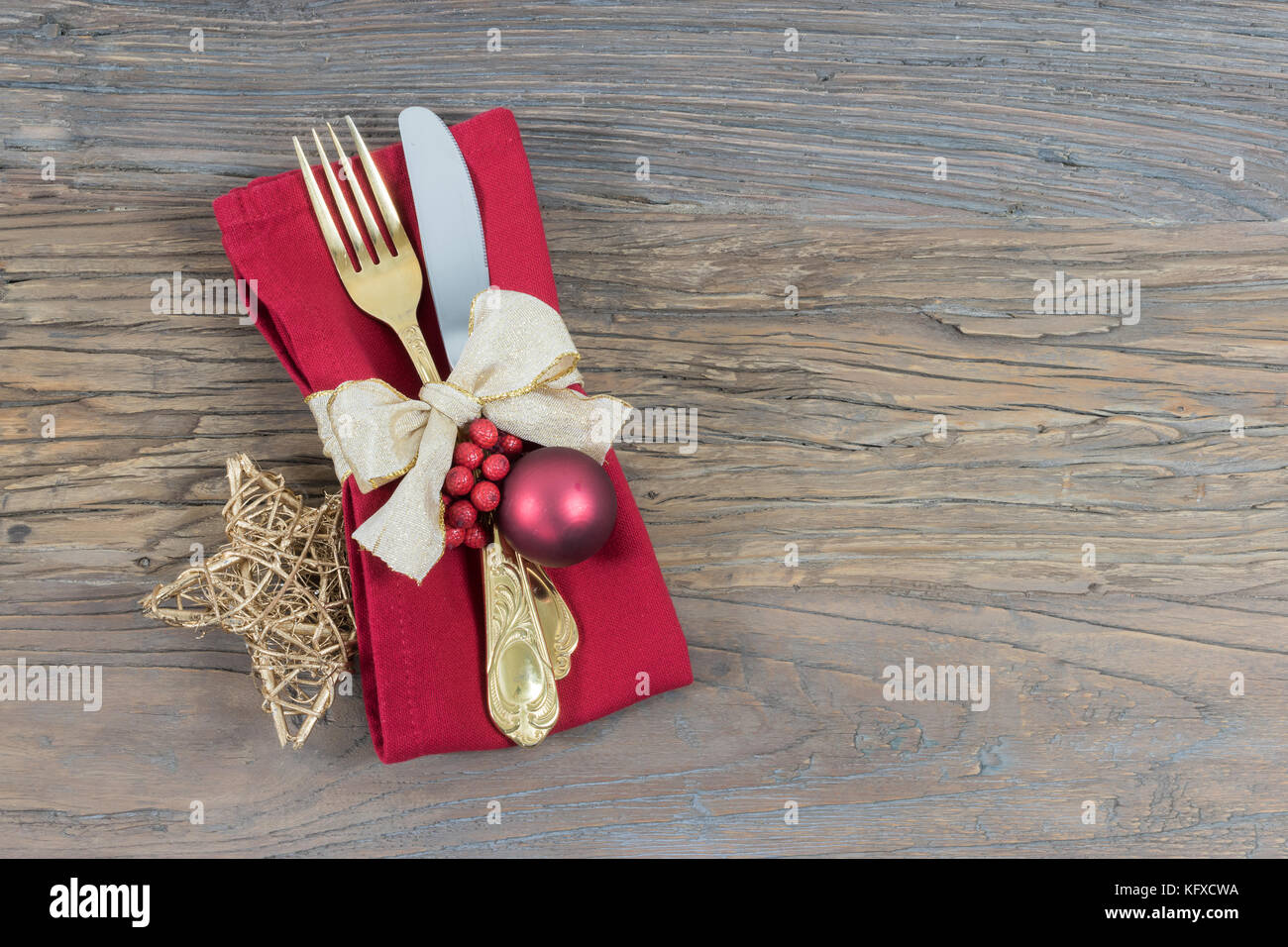 Christmas table place setting. Holidays background. Gold cutlery , red napkin, and glittering star with festive ribbon on rustic wood. Stock Photo