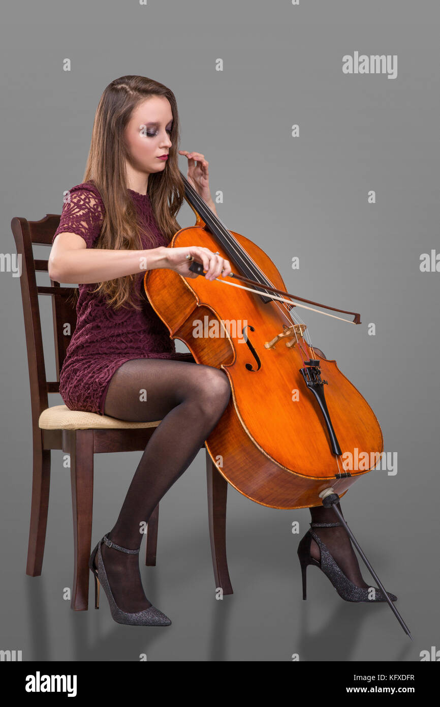 Beautiful young woman sitting on the chair and playing cello. Isolated