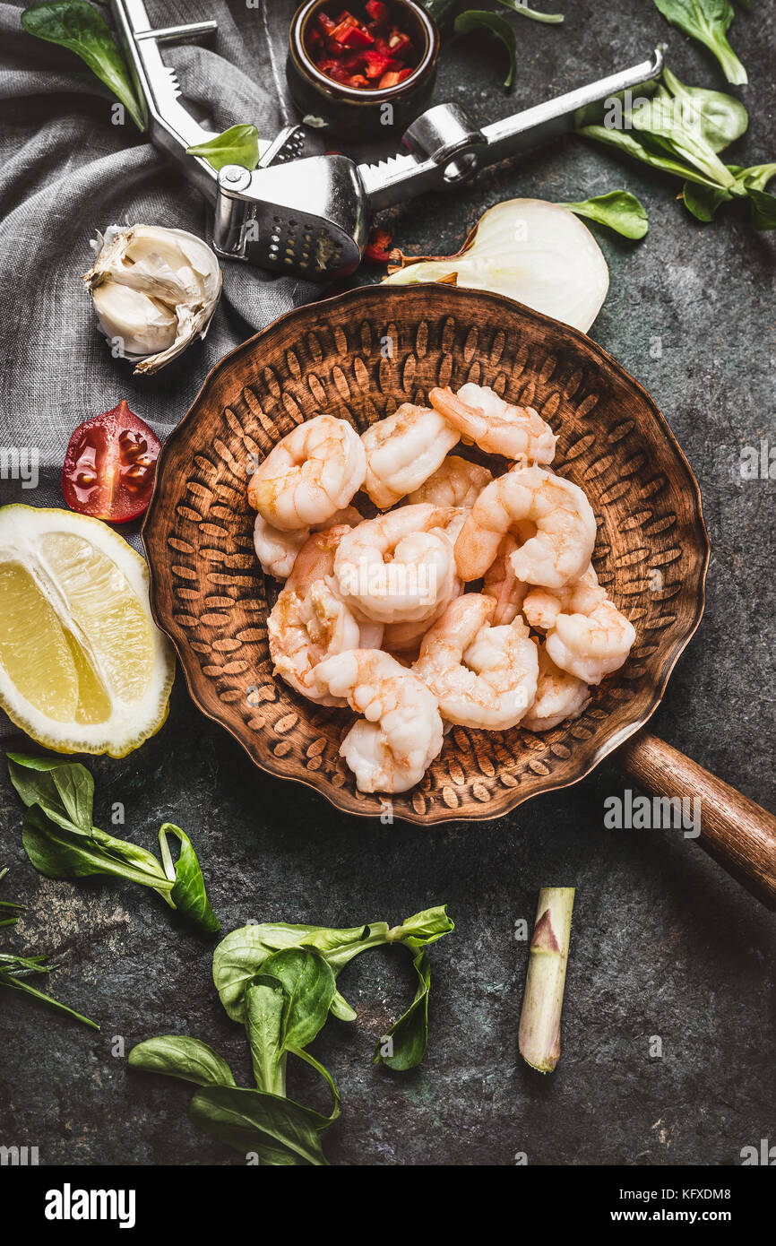 Shrimps in fried pan on rustic  kitchen table background with cooking ingredients, top view Stock Photo