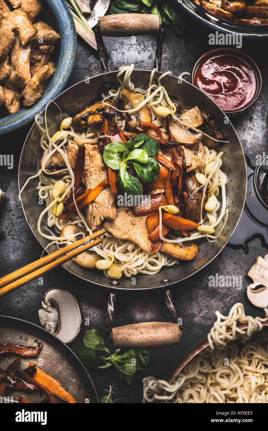 Asian dish with chicken vegetables noodle stir-fry in little wok with chopstick and cooking ingredients, top view Stock Photo