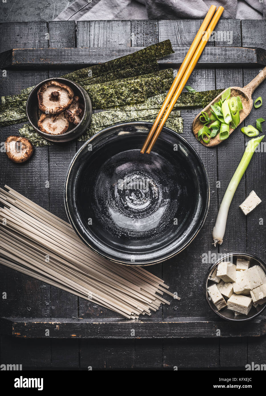 Miso soup preparation with cooking ingredients: udon noodles, tofu,  Shiitake Mushrooms , nori and green onion on dark rustic background, top view Stock Photo