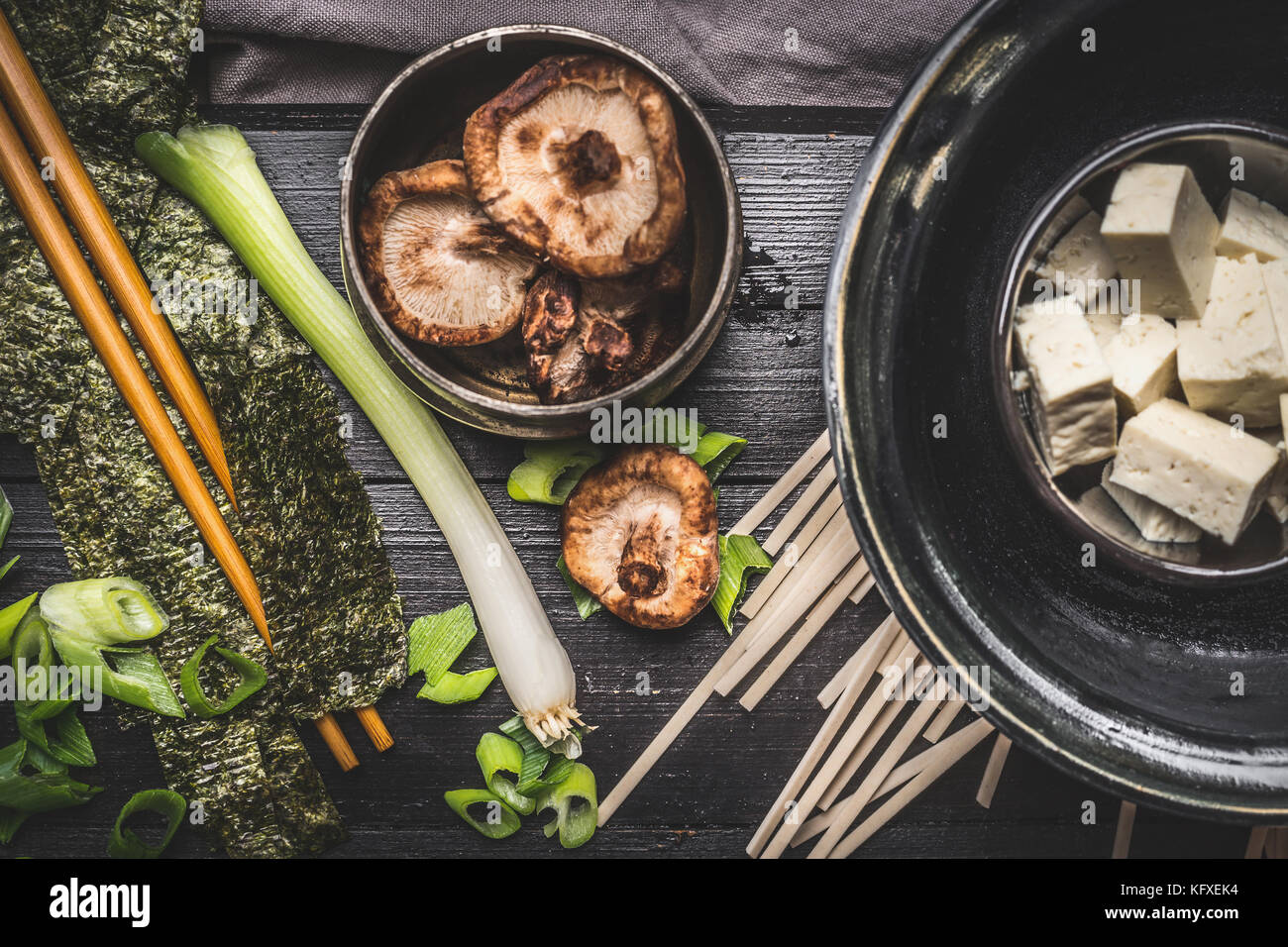 Cooking ingredients for asian soup: udon noodls, tofu,  Shiitake Mushrooms , nori and green onion on dark rustic background, top view Stock Photo