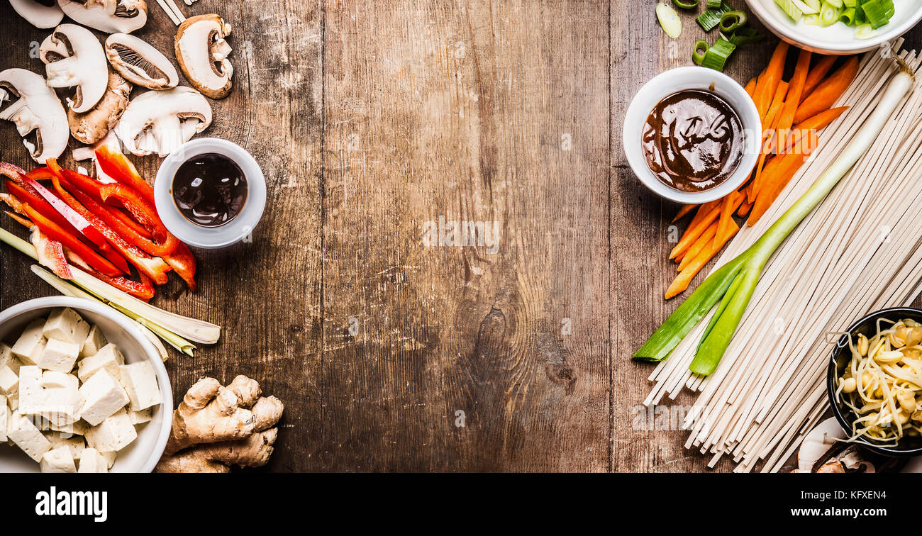 Asian vegetarian cooking ingredients for stir fry with tofu, noodles , vegetables and sauces on wooden rustic background, top view, banner, frame Stock Photo