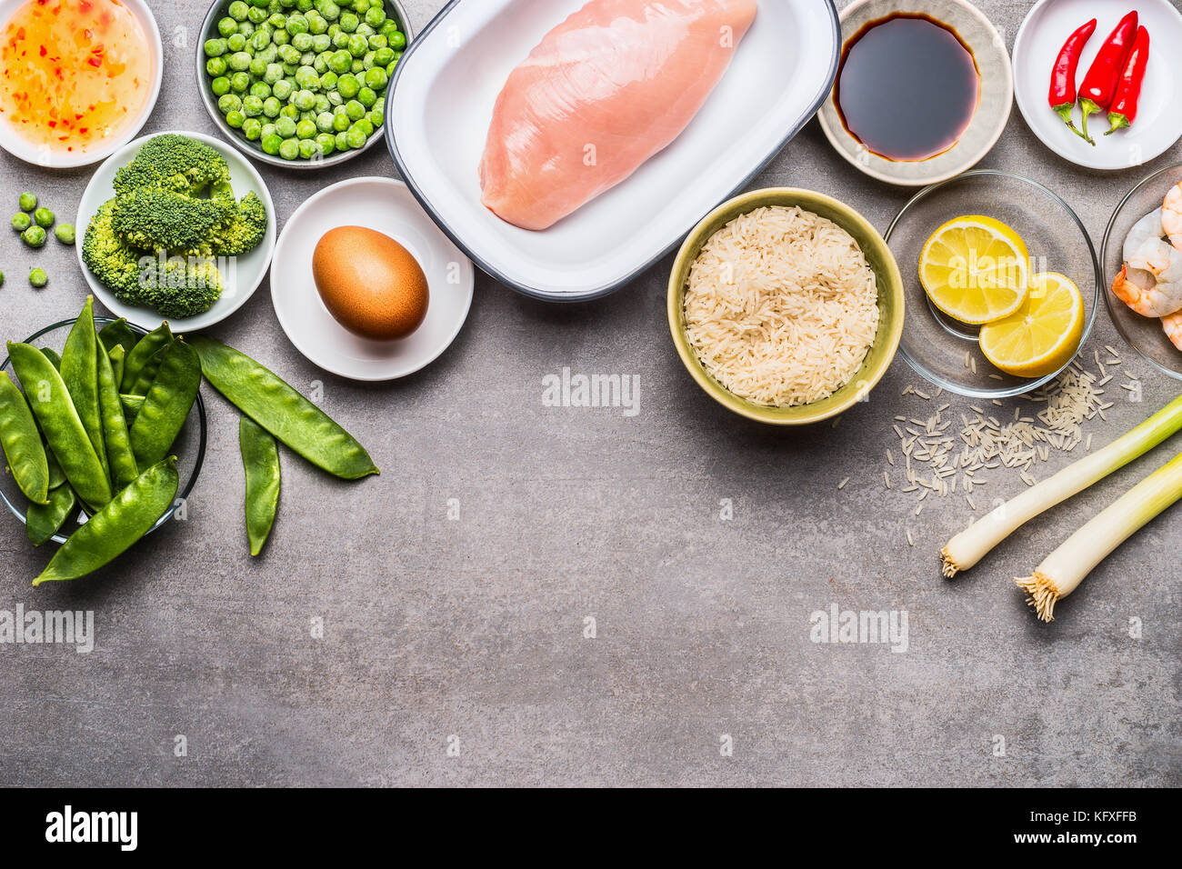 Asian fried rice cooking ingredients with chicken , egg , shrimps and green vegetables  on gray stone background, top view, border Stock Photo