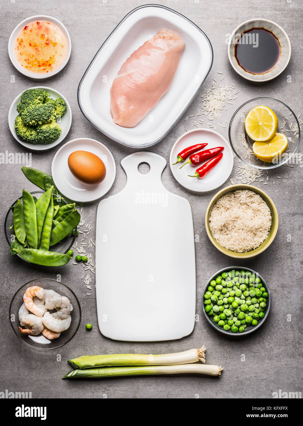 Fried rice cooking ingredients with chicken , egg , shrimps and green vegetables around white cutting board  on gray stone background  , top view Stock Photo