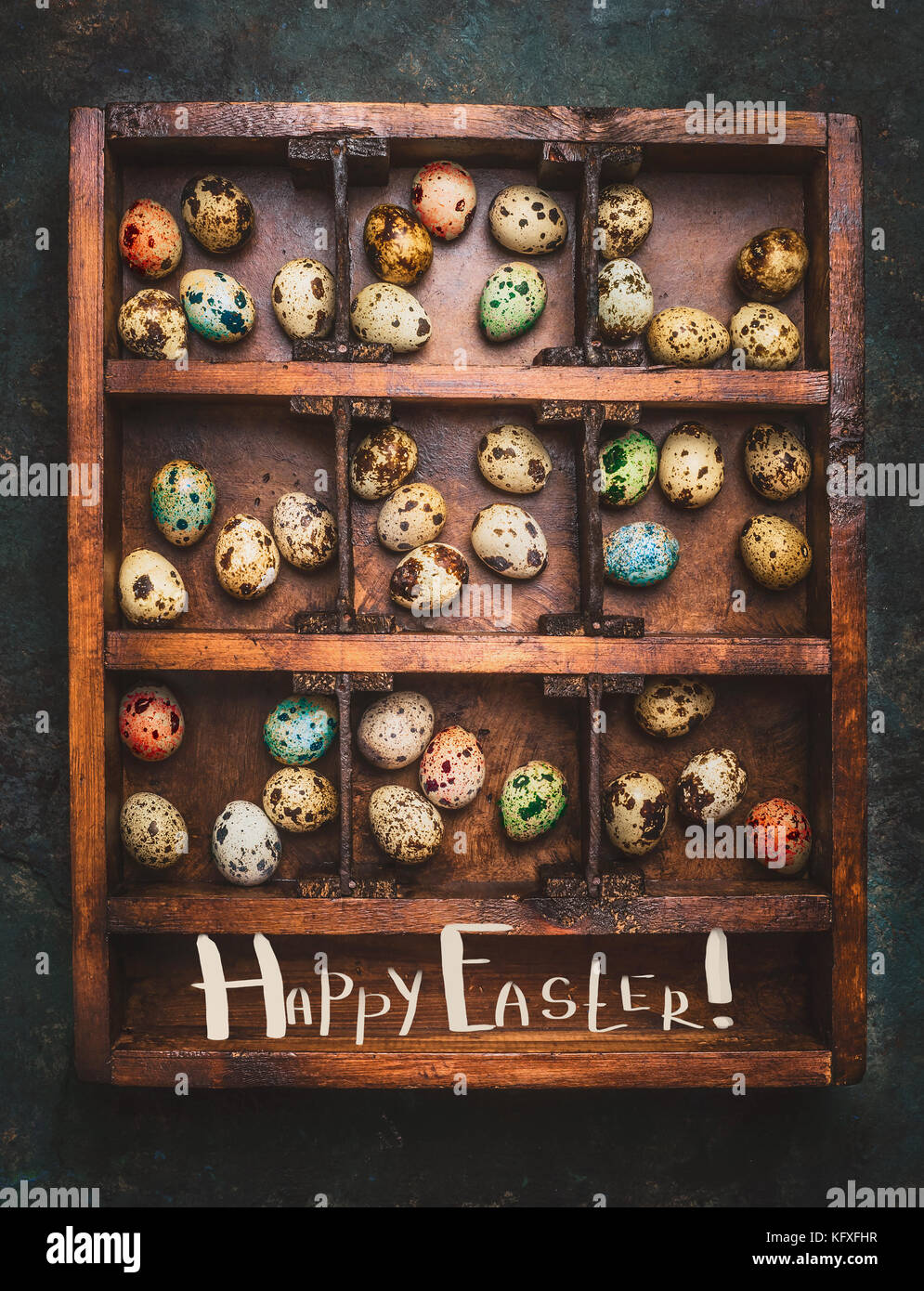 Colored eggs for Easter feast in aged Wooden box on dark rustic background with lettering Happy Easter, top view Stock Photo