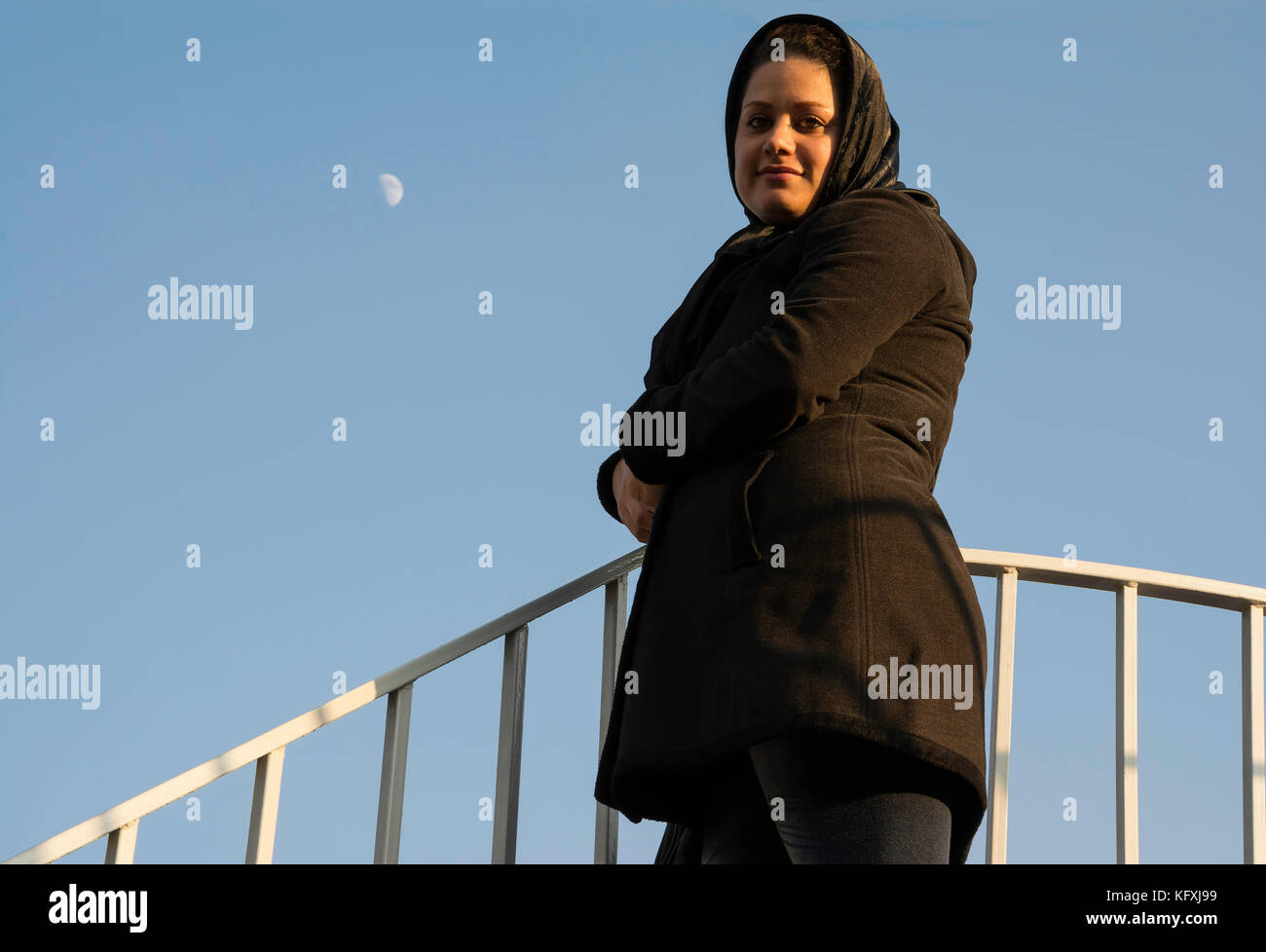 Portrait of a Muslim Woman with Golden Sunlight on Her Face in Front of Blue Sky with Moon Planet at Background. Stock Photo