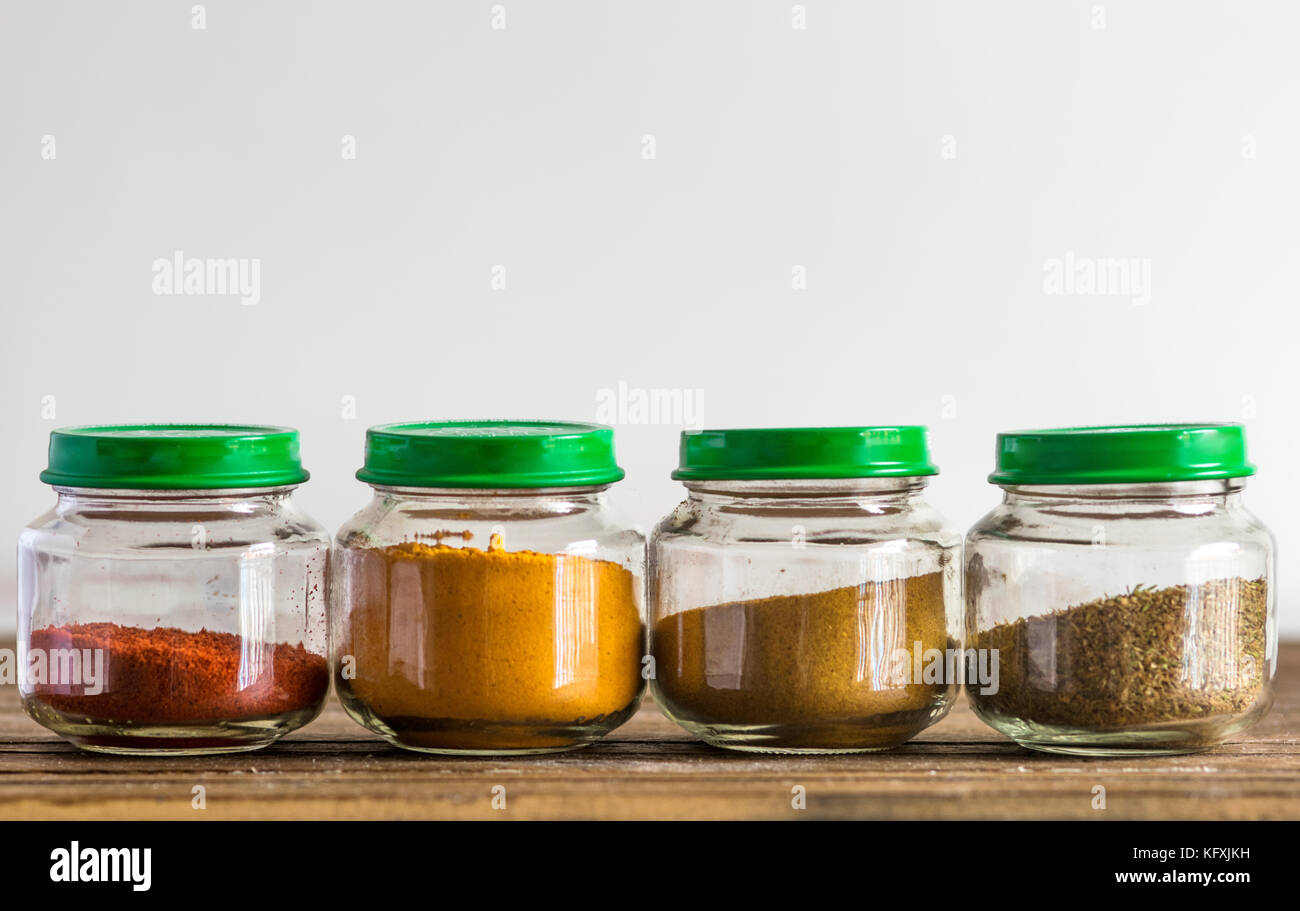 Spices and seasoning containers, glass pots and bowls in a row, on a wooden surface and white background Stock Photo