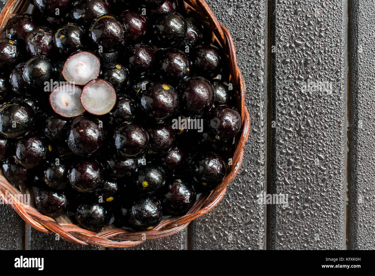 Jabuticabas, also known as Brazilian Berry or Brazilian Grapetree (Plinia cauliflora) fruits on a wooden vine basket, with a black wooden background Stock Photo
