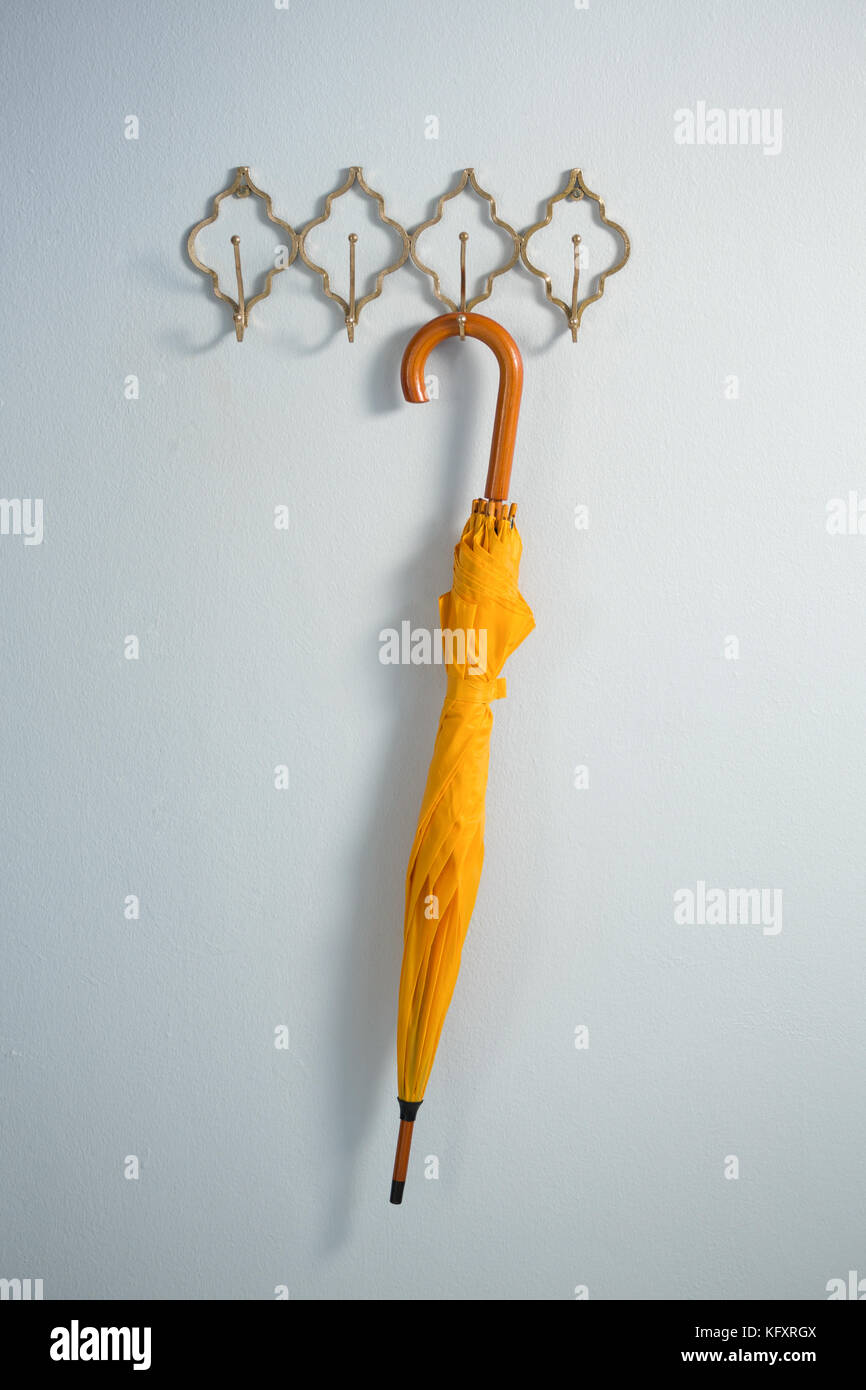 Yellow umbrella hanging on hook against white wall Stock Photo Alamy