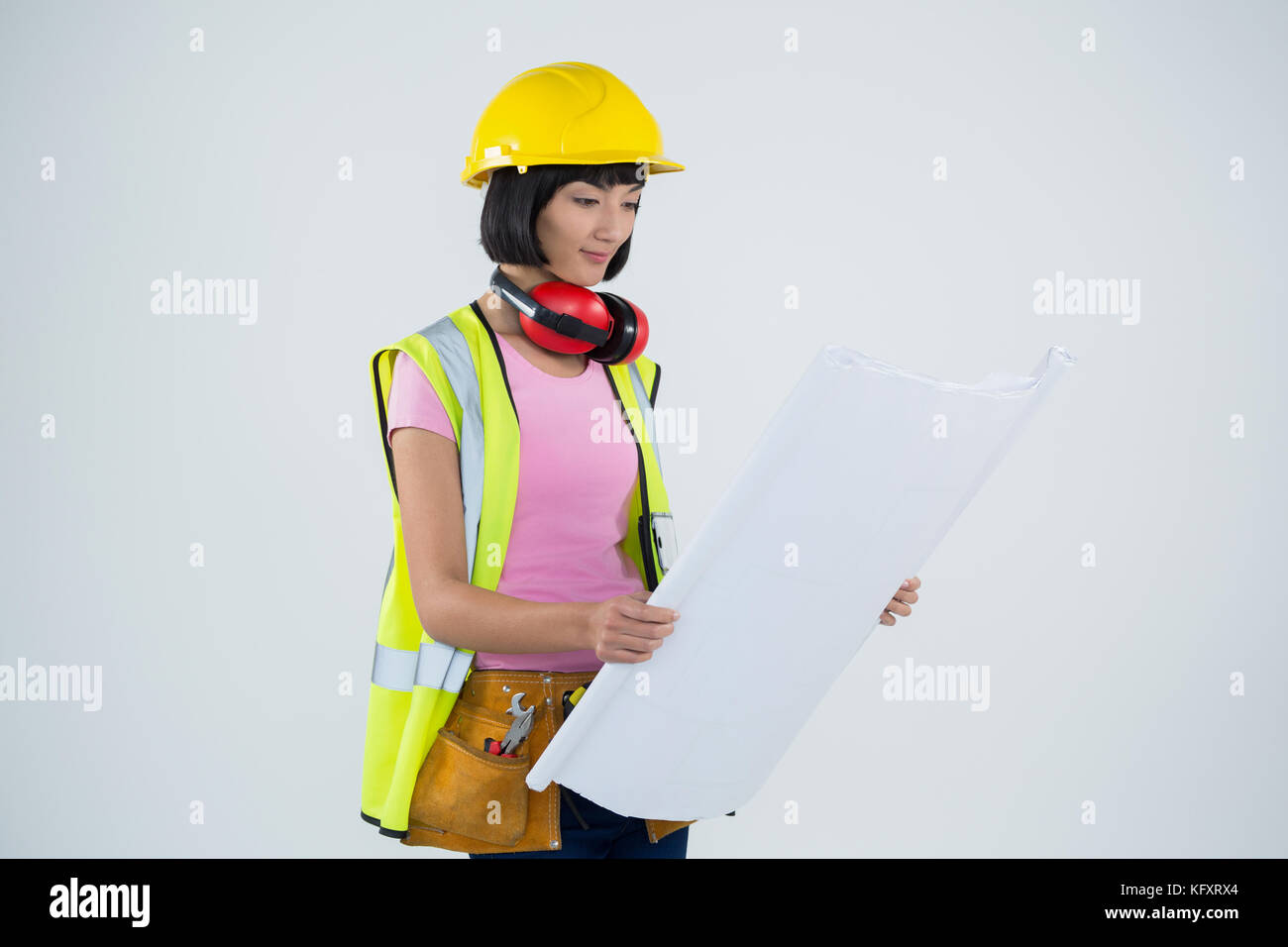 Smiling female architect looking at blueprint against white background ...