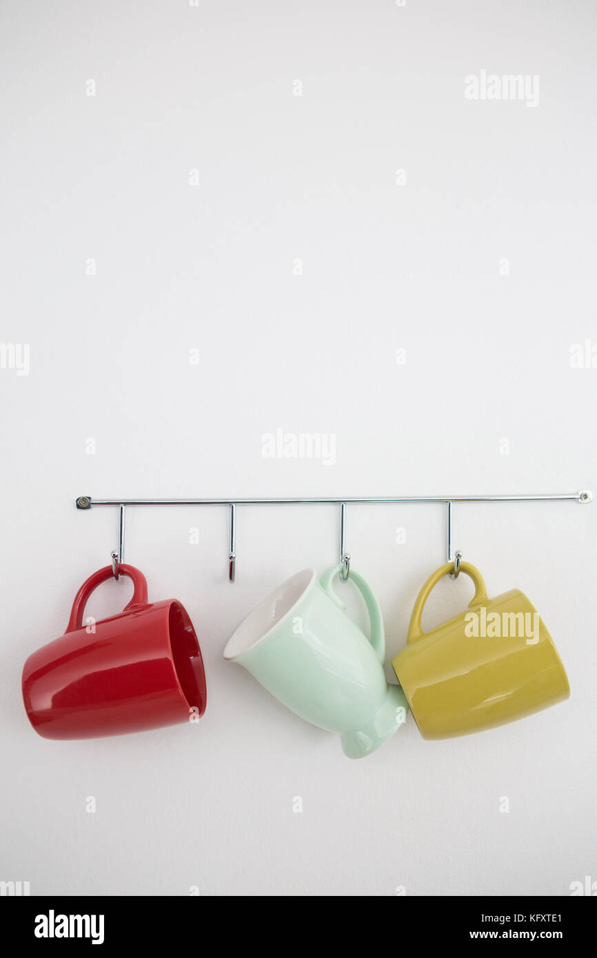 Colorful mugs hanging on hook against white wall Stock Photo Alamy