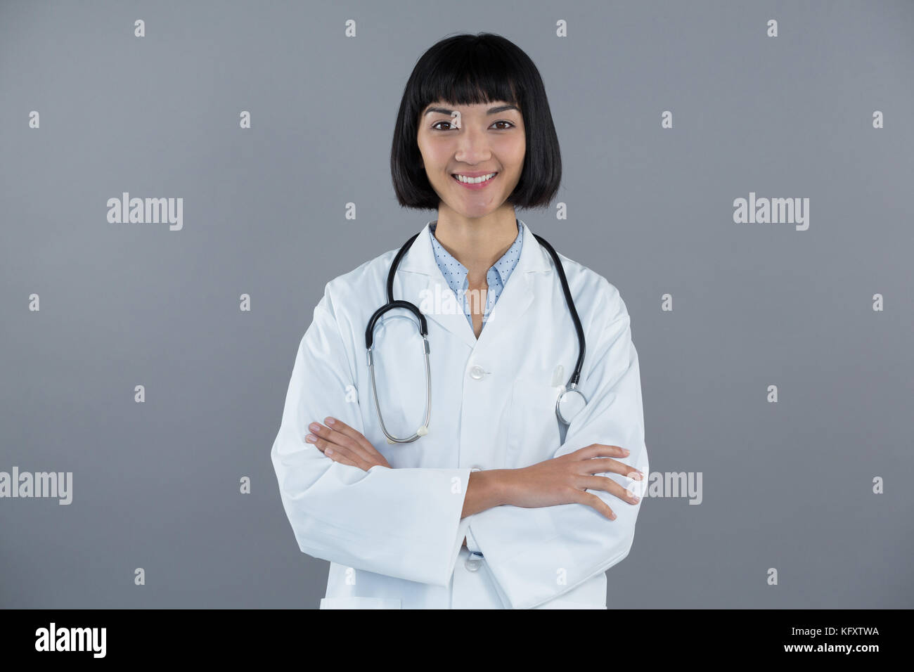 Portrait of doctor standing with arms crossed against grey background ...