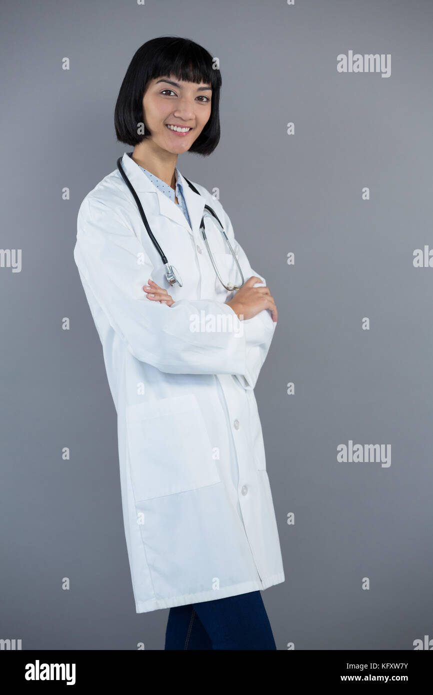 Portrait of doctor standing with arms crossed against grey background ...