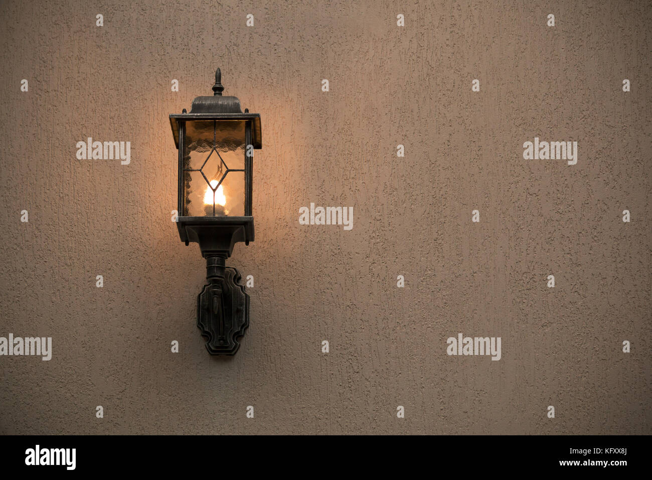 A yellow glass lantern hanging on a gray old wall. Bright glowing lantern illuminating the wall of an ancient building Stock Photo