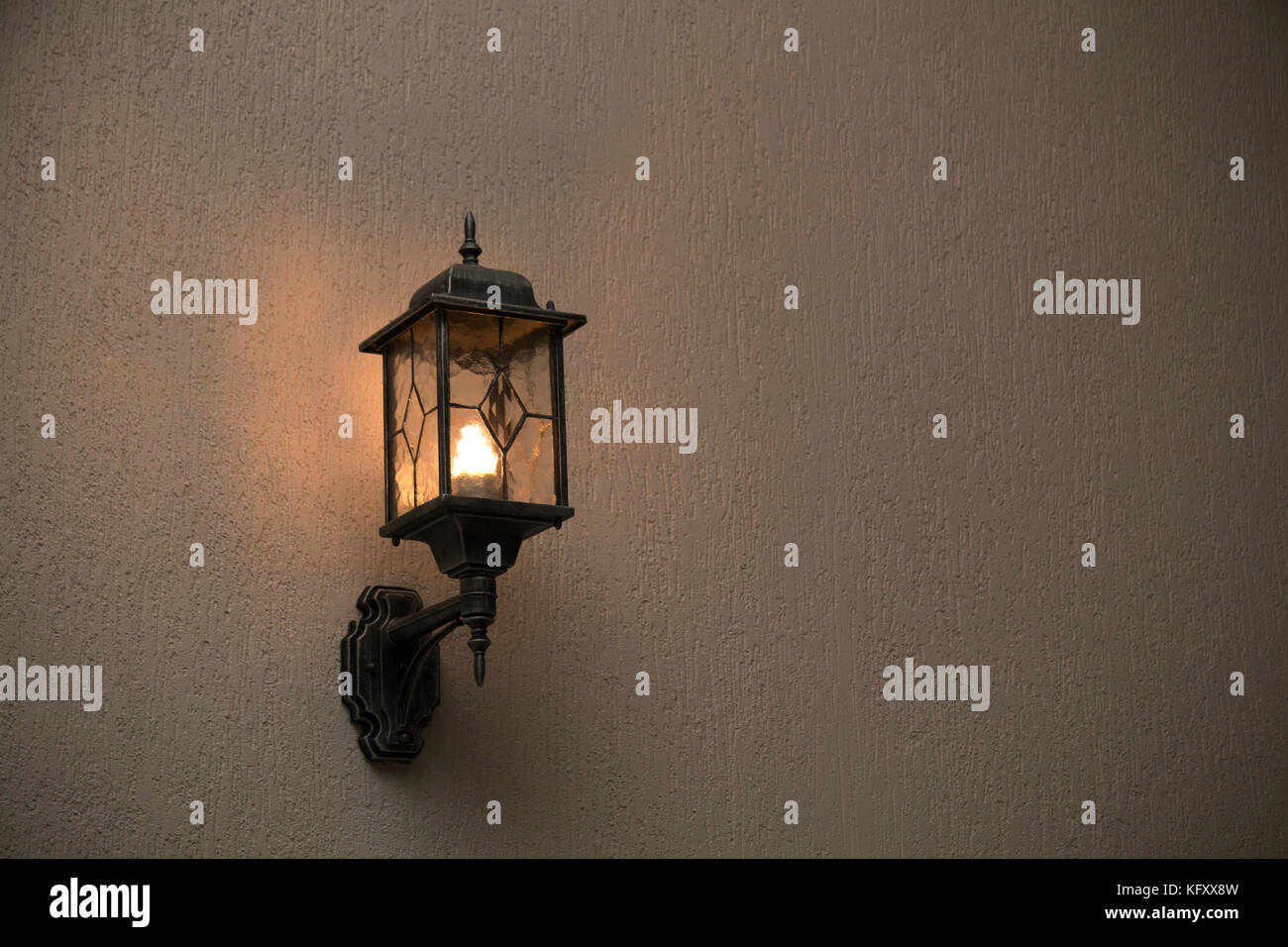 A yellow glass lantern hanging on a gray old wall. Bright glowing lantern illuminating the wall of an ancient building Stock Photo