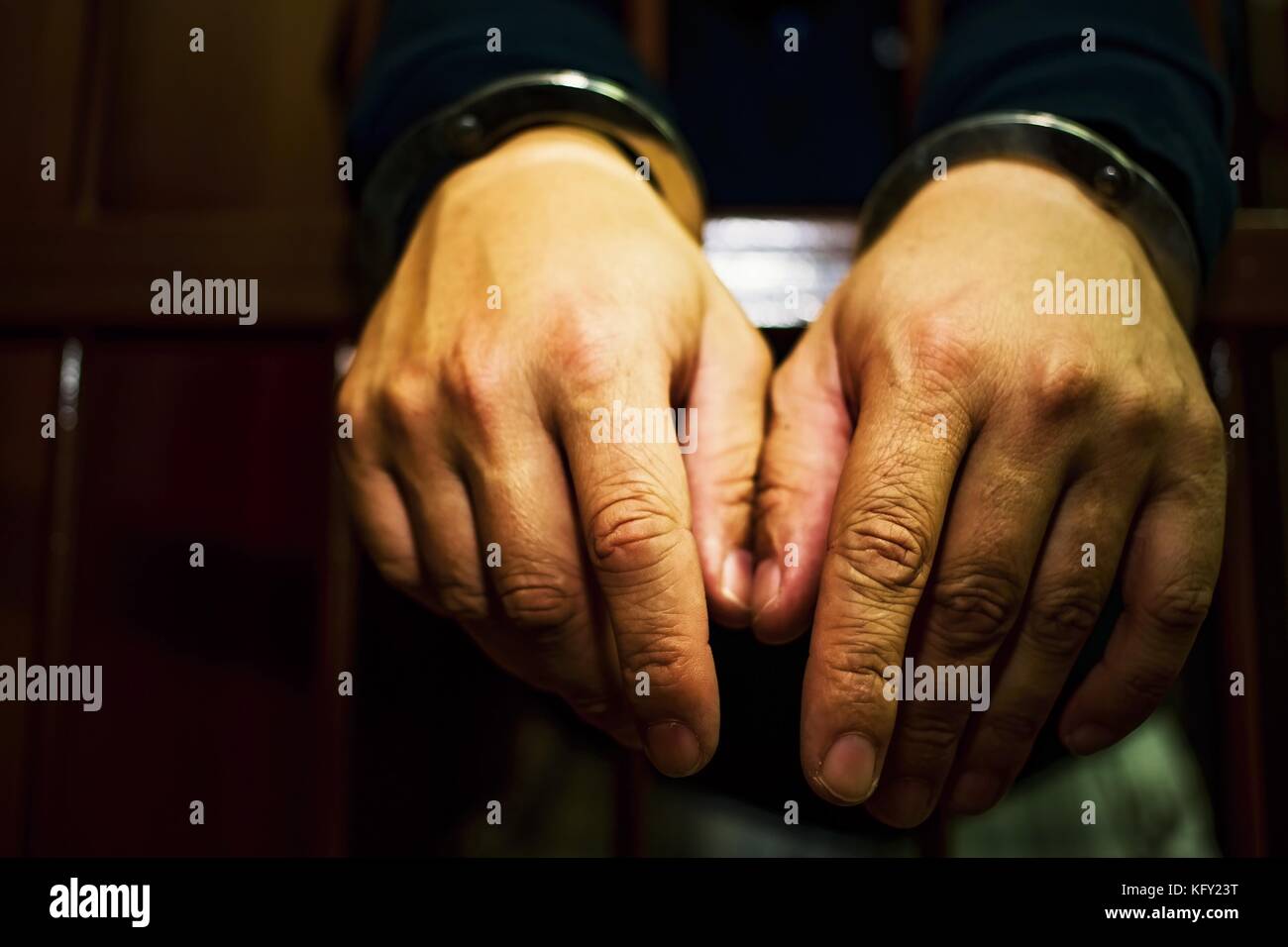 Abstract. Hands of the prisoner on a steel lattice close up. Prison, man in handcuffs. Detail of hands with steel handcuffs. Stock Photo